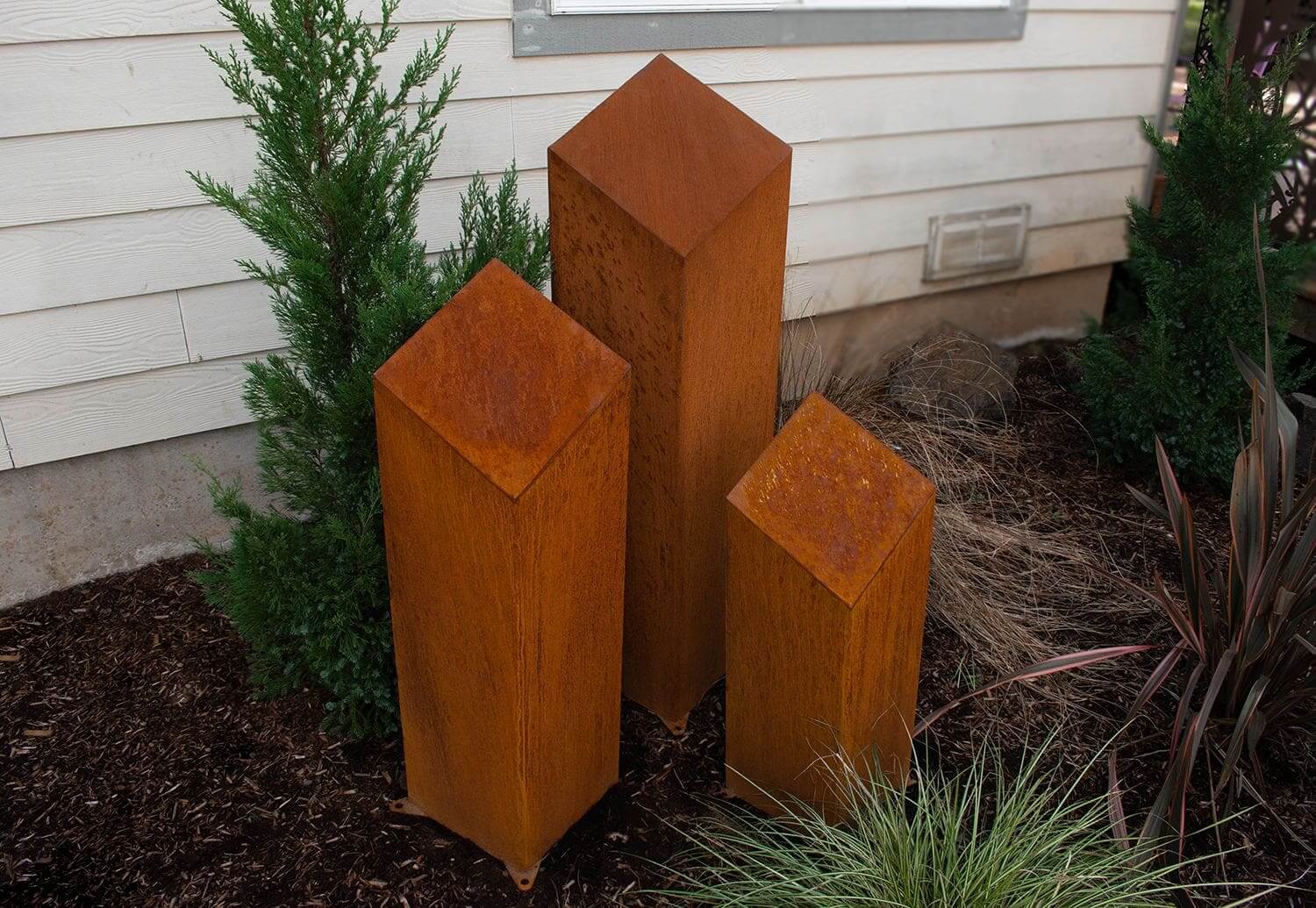 Three rusted metal sculptures in a garden.