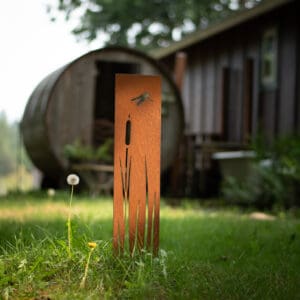 A metal sculpture in the grass near some buildings.