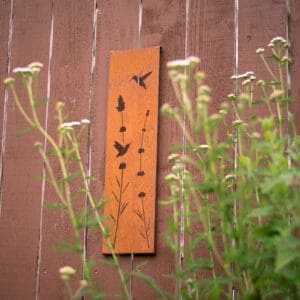 A wooden sign with birds flying above some flowers.