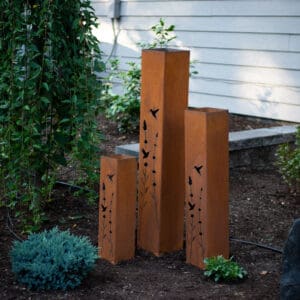 A group of three metal sculptures in the middle of a garden.