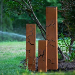 Three wooden posts in the grass near a tree.