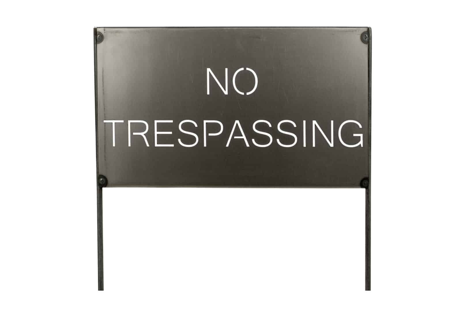 Black 'No Trespassing' metal sign on stakes